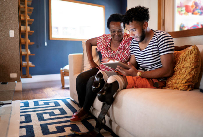 A man with prosthetic legs and his mother using a tablet while sitting on couch